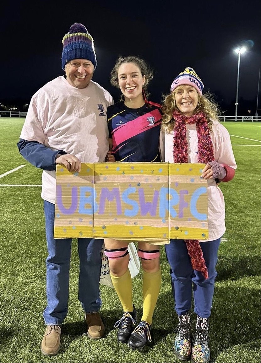 Eliza with two supporters holding a rugby sign at night.